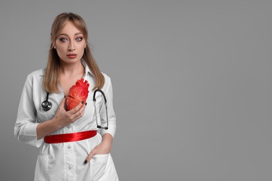 Photo of Woman in scary nurse costume with heart model on light grey background, space for text. Halloween celebration