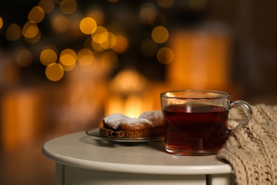 Cup of hot tea on white table against blurred lights, space for text. Cozy winter