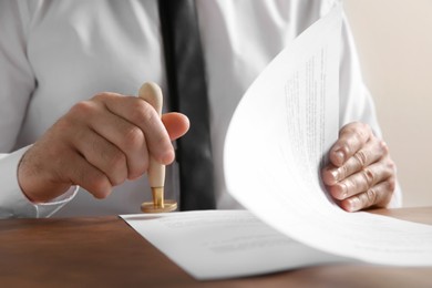 Photo of Male notary stamping document at table, closeup