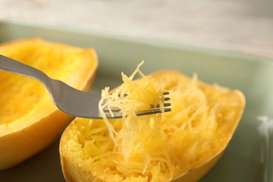 Photo of Fork with flesh over cooked spaghetti squash in baking dish, closeup