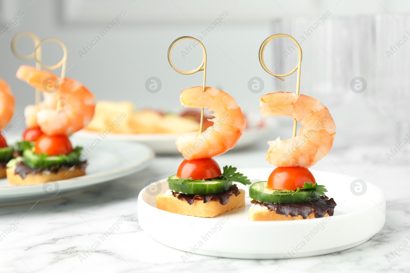 Photo of Tasty canapes with shrimps, cucumber, greens and tomatoes on white marble table, closeup