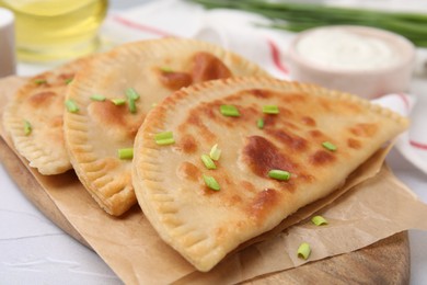 Photo of Delicious fried chebureki with cheese and green onion on white textured table