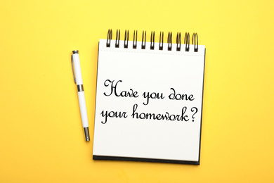 Image of Pen and stylish notebook with phrase HAVE YOU DONE YOUR HOMEWORK? on yellow background, top view