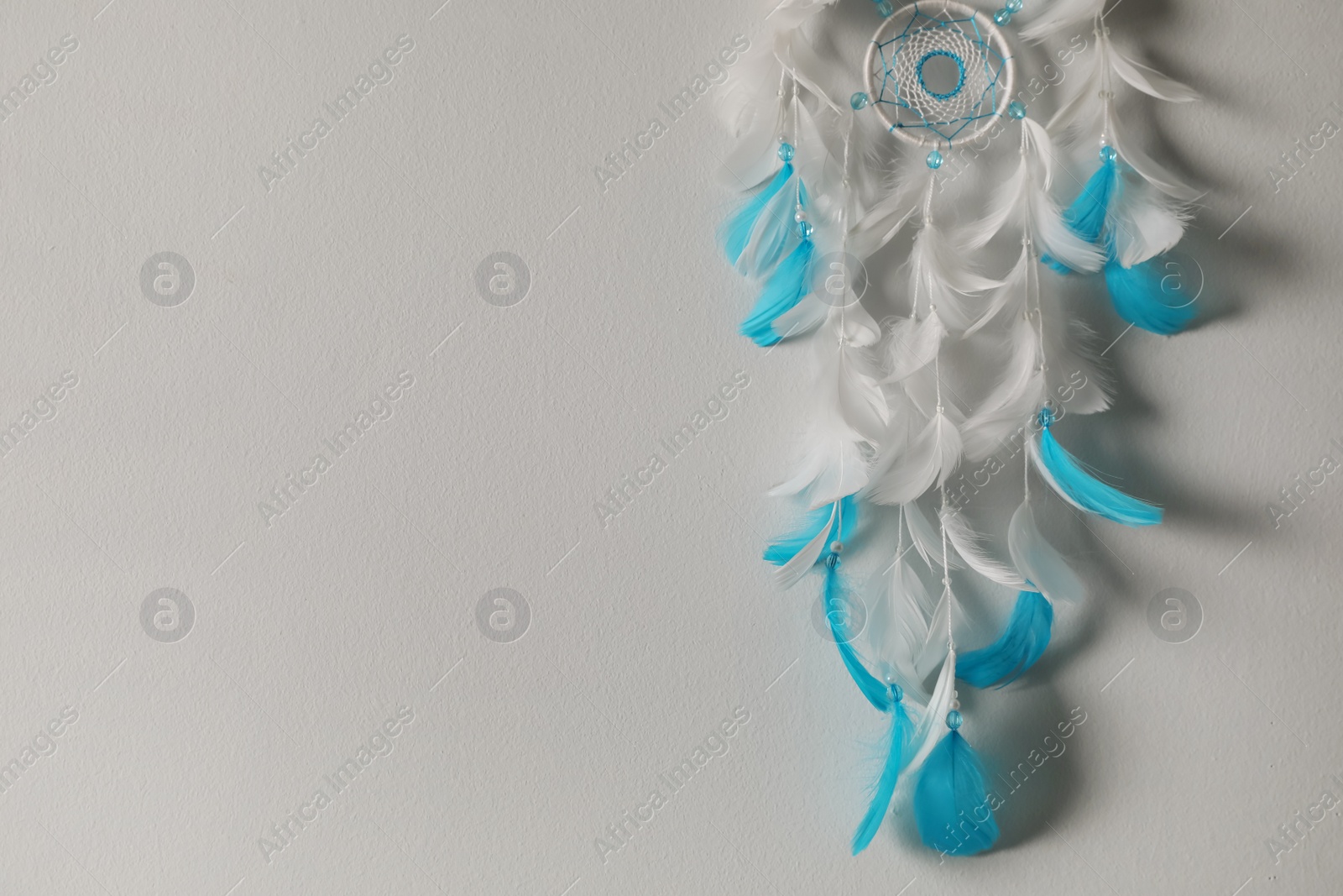 Photo of Beautiful dream catcher hanging on white wall. Space for text