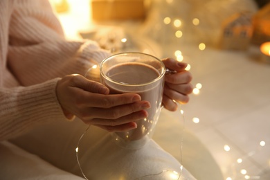 Photo of Woman with cup of drink and blurred Christmas lights on background, closeup