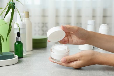 Photo of Woman holding jar of hemp cream at light table, closeup. Natural cosmetics