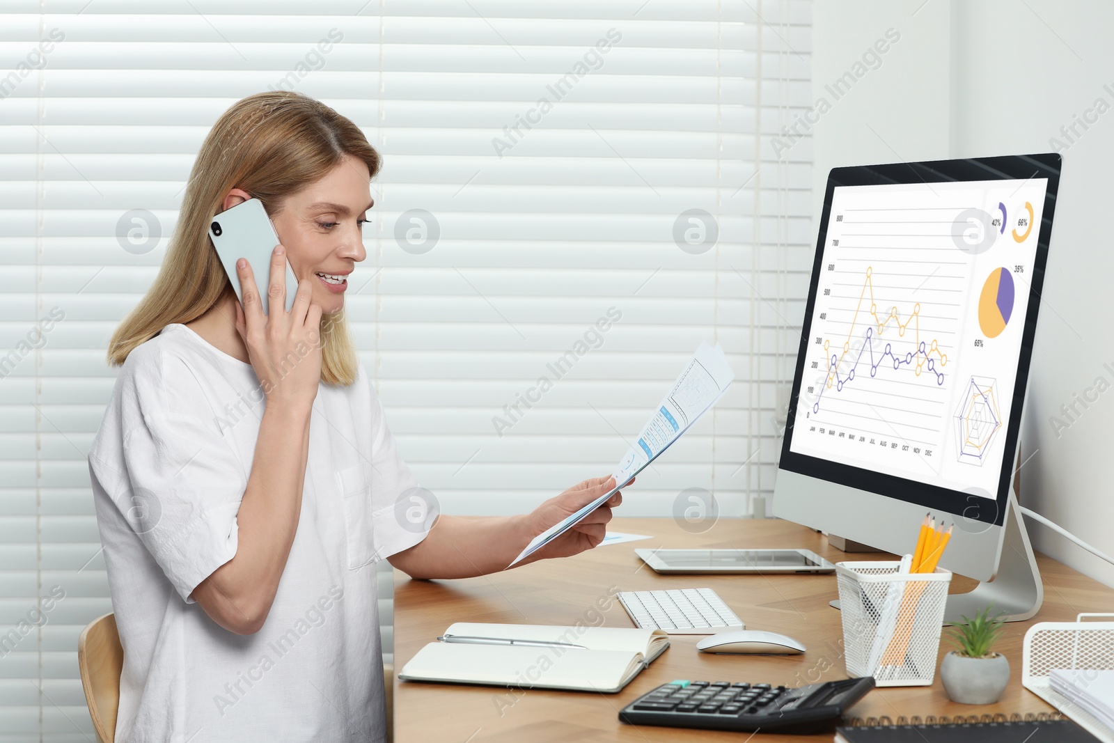 Photo of Professional accountant talking on phone while working at wooden desk in office