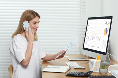 Professional accountant talking on phone while working at wooden desk in office