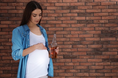 Photo of Future mother with bottle of alcohol drink against brick wall. Bad habits during pregnancy