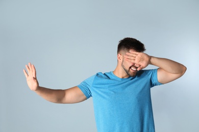 Young man being blinded on grey background