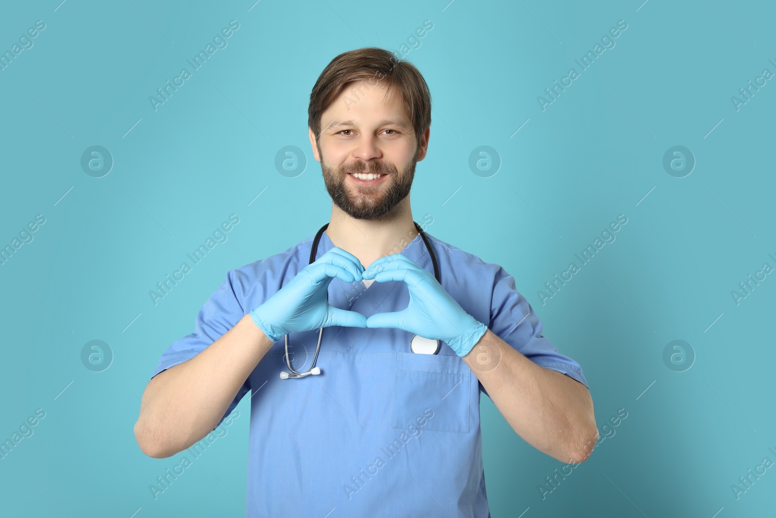 Photo of Doctor or medical assistant (male nurse) making heart with hands on turquoise background