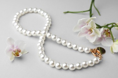 Photo of Elegant pearl necklace and orchid flowers on white background, closeup