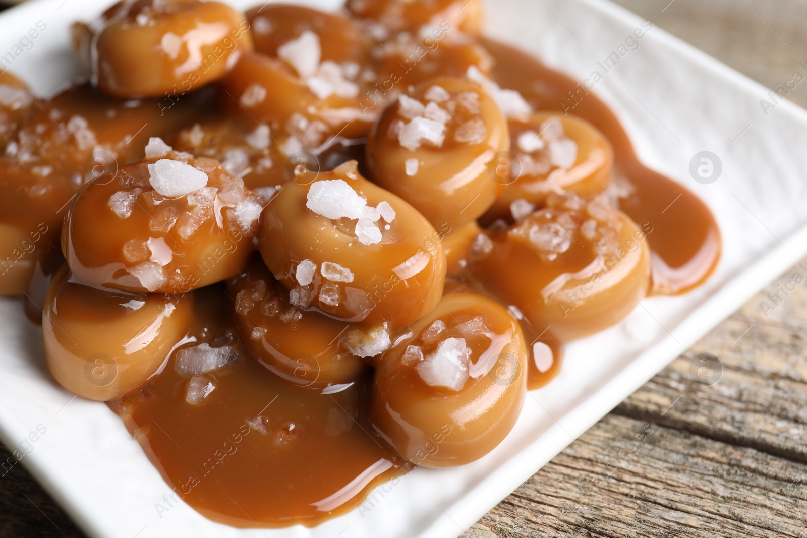 Photo of Tasty candies, caramel sauce and salt on wooden table, closeup