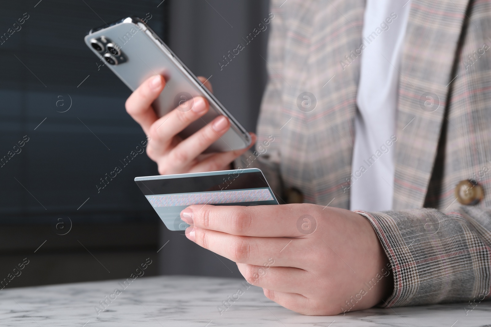 Photo of Online payment. Woman with smartphone and credit card at white marble table, closeup