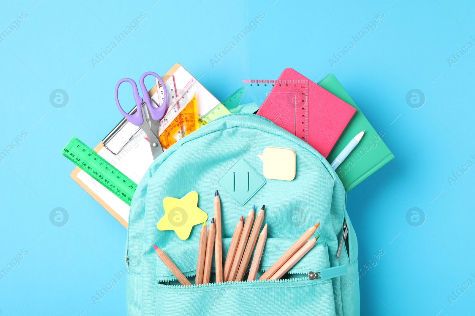 Photo of Stylish backpack with different school stationery on light blue background, top view. Back to school