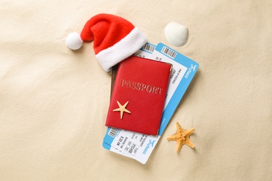 Photo of Passport with tickets and Santa hat, seashell, starfish on sand, flat lay. Christmas vacation