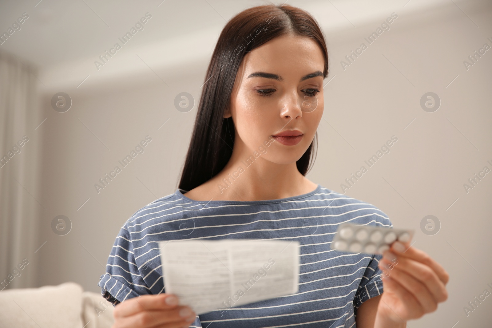 Photo of Young woman with pills reading medicine instruction indoors