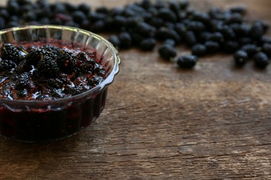Bowl of sweet black mulberry jam on wooden table, space for text