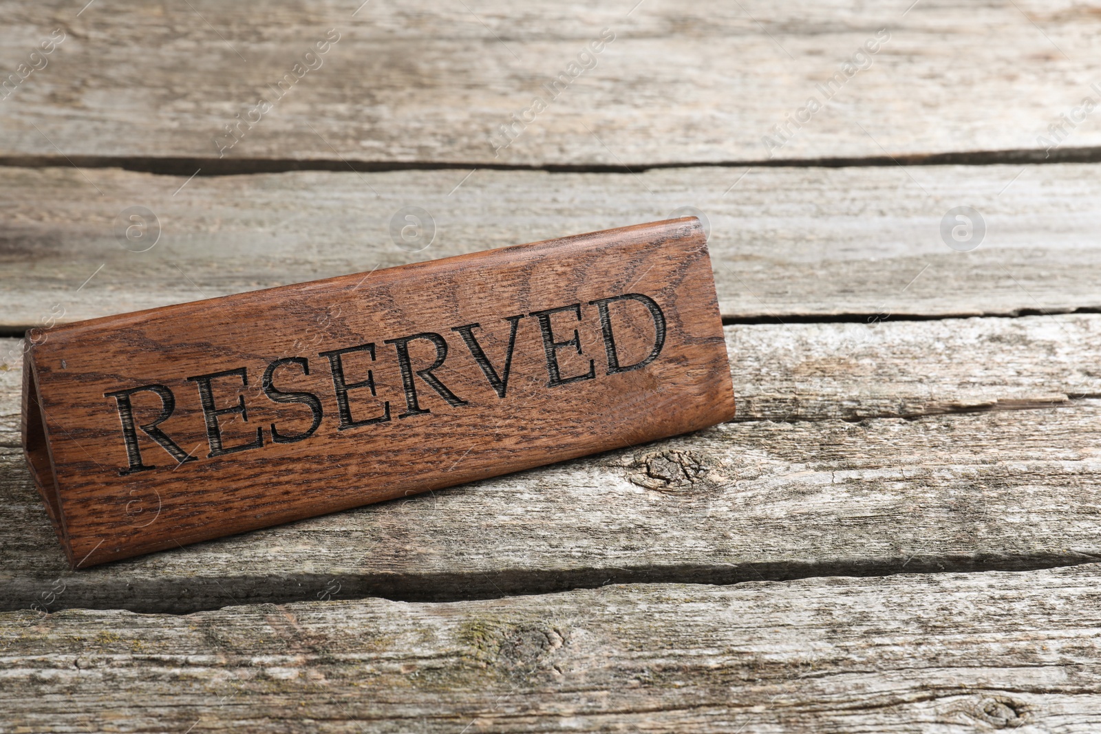 Photo of Elegant sign RESERVED on wooden surface, space for text. Table setting element