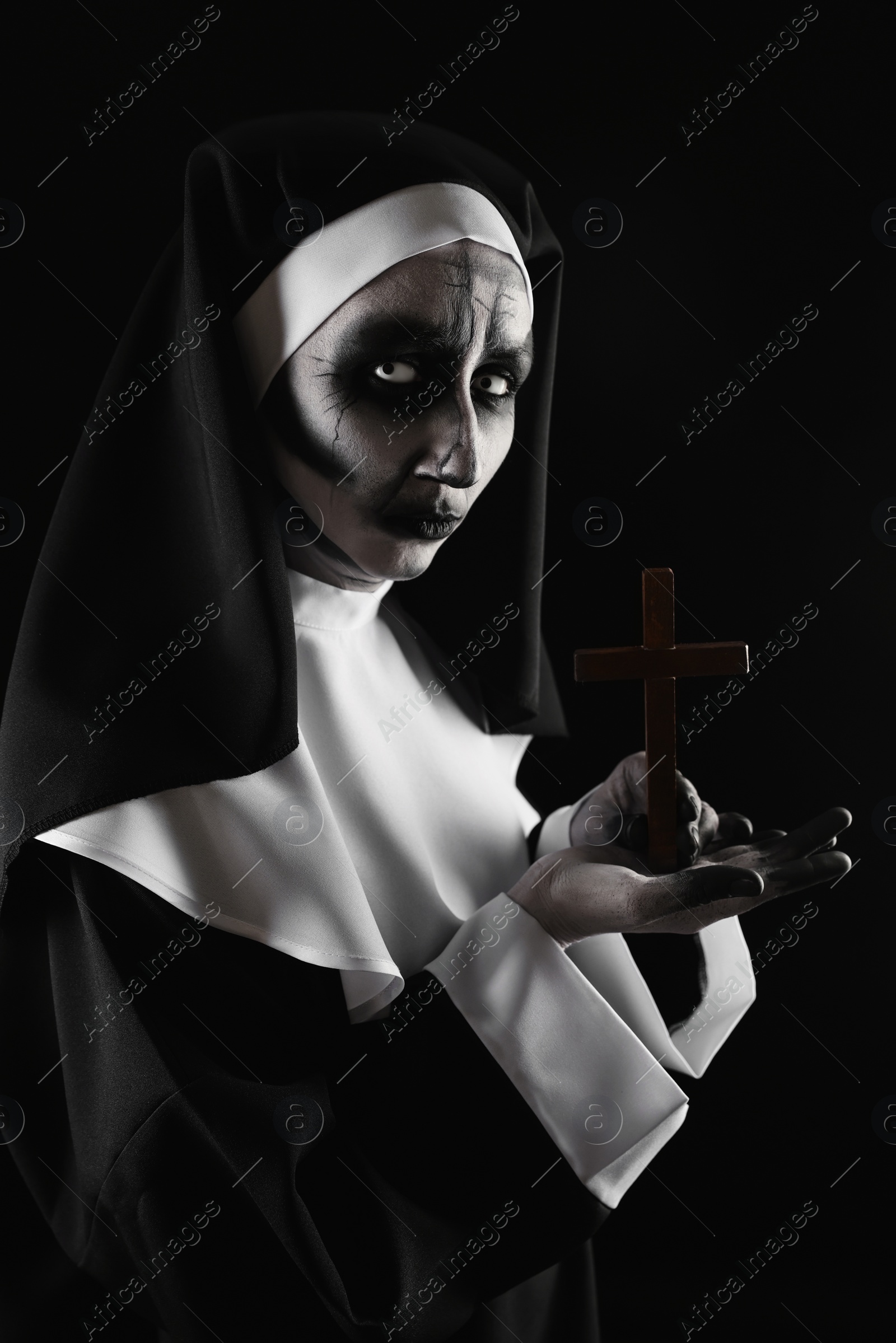 Photo of Scary devilish nun with cross on black background. Halloween party look