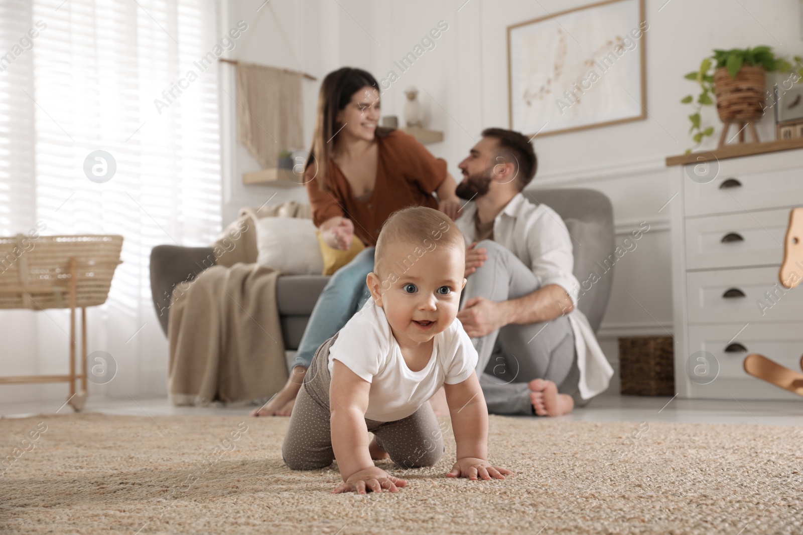 Photo of Happy parents watching their baby crawl on floor at home