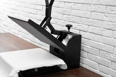 Photo of Heat press machine with t-shirt on wooden table near white brick wall