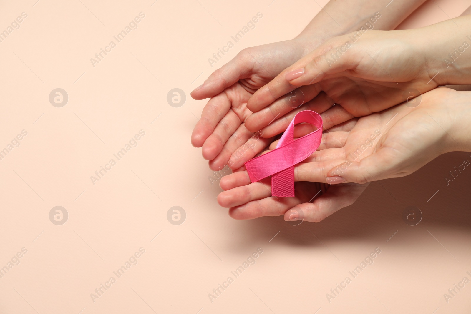 Photo of Breast cancer awareness. Women holding pink ribbon on beige background, top view. Space for text