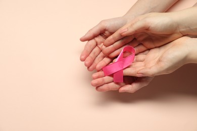 Photo of Breast cancer awareness. Women holding pink ribbon on beige background, top view. Space for text