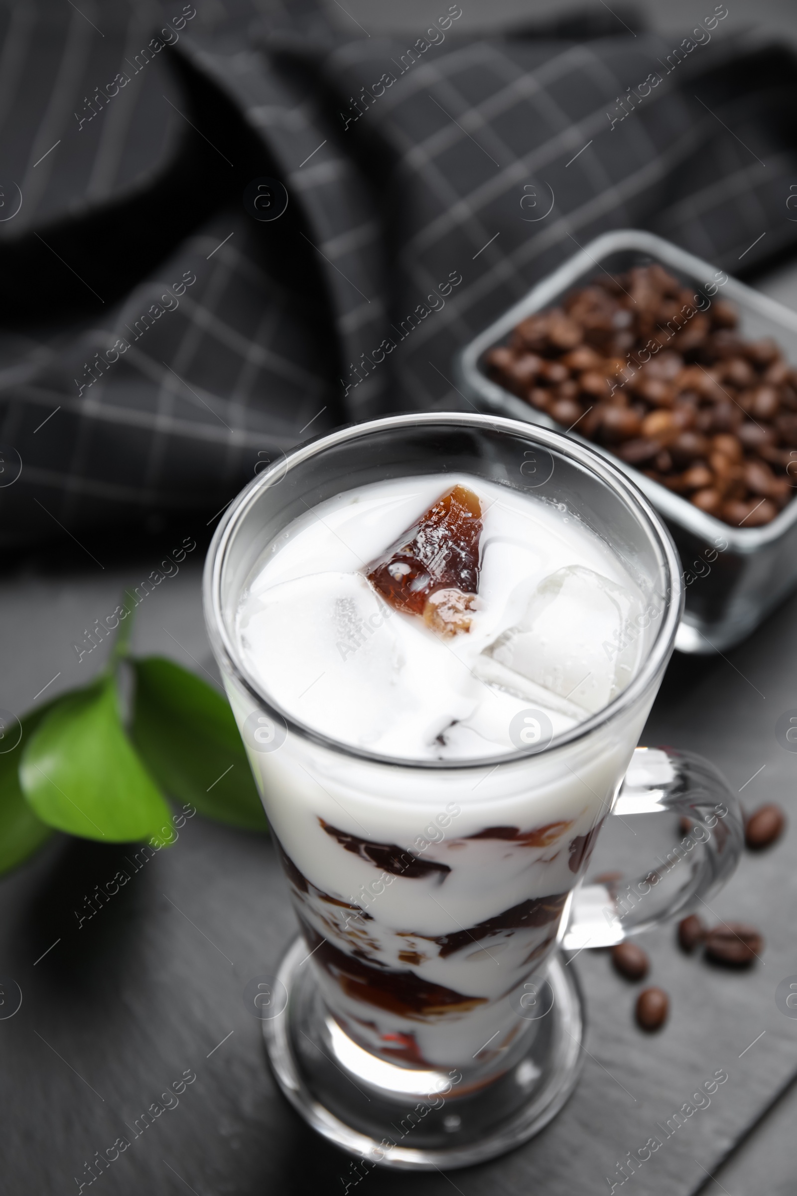 Photo of Glass cup of milk with delicious grass jelly and coffee beans on black table, closeup