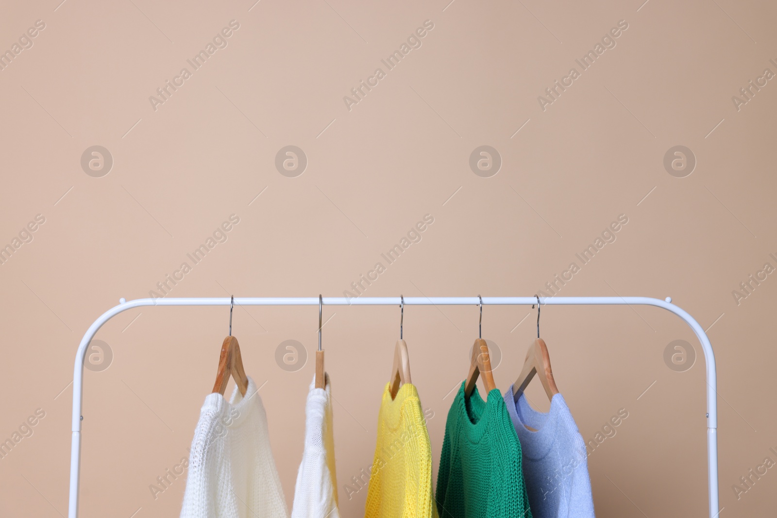 Photo of Rack with different warm sweaters on beige background. Space for text