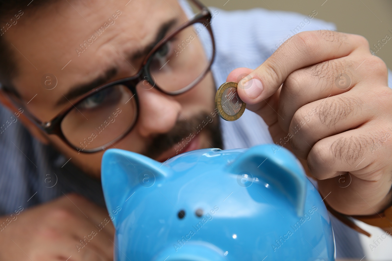 Photo of Young man putting coin into piggy bank, focus on hand. Money savings