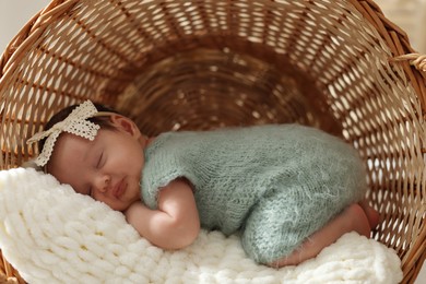 Adorable newborn baby sleeping in wicker basket with soft plaid