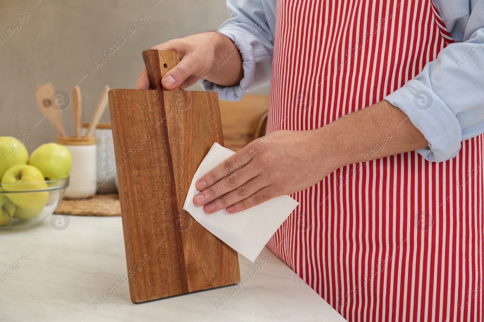 Photo of Man wiping wooden cutting board with paper napkin at white table, closeup