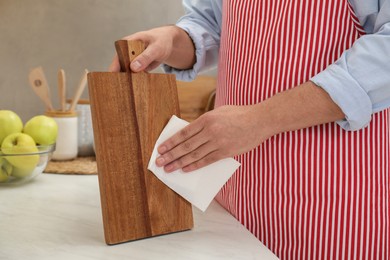 Man wiping wooden cutting board with paper napkin at white table, closeup