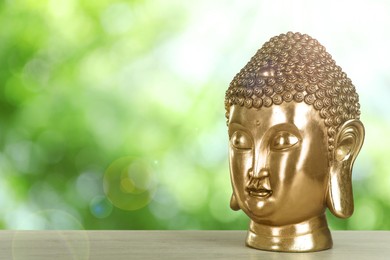 Golden Buddha sculpture on wooden table outdoors. Space for text