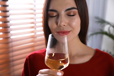 Beautiful young woman with glass of luxury white wine indoors, closeup view