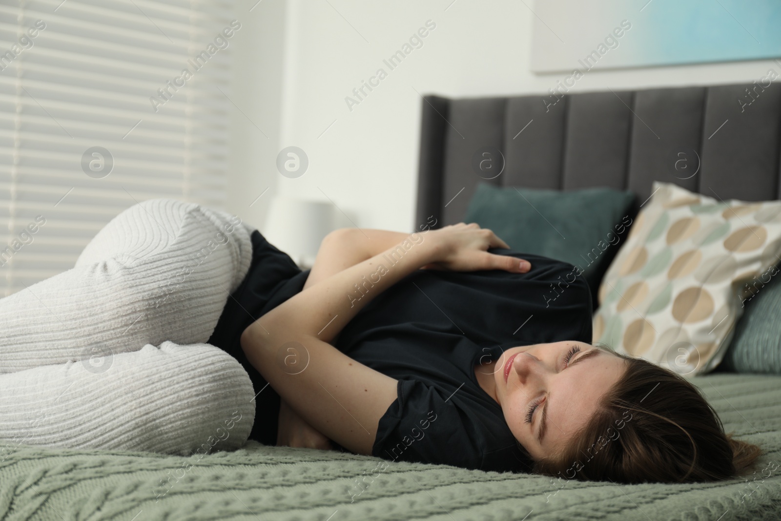 Photo of Sad young woman lying on bed at home