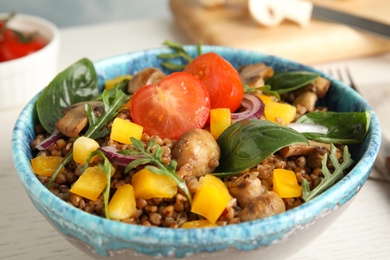 Delicious buckwheat porridge with vegetables and mushrooms on wooden table, closeup