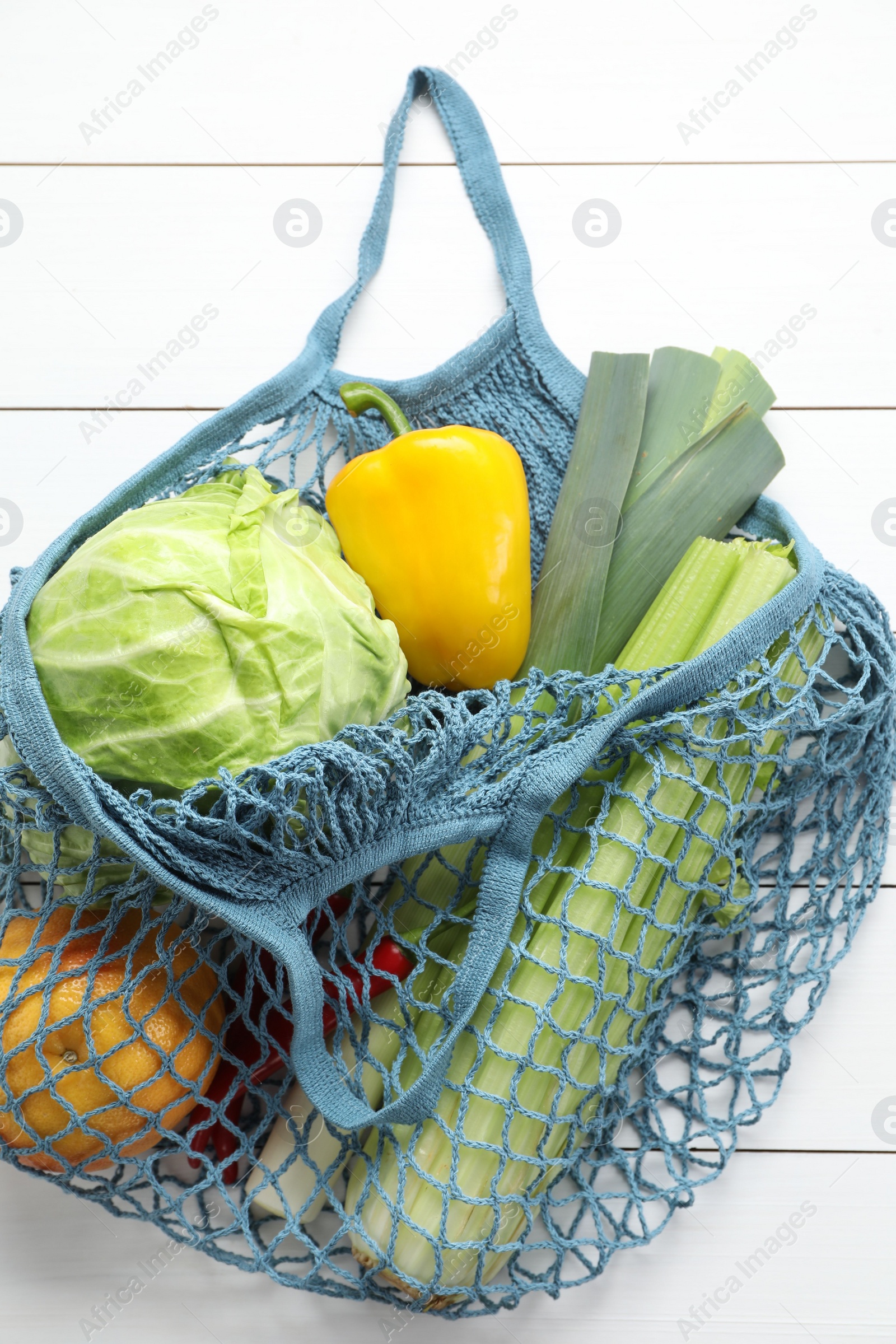 Photo of String bag with different vegetables on white wooden table, top view