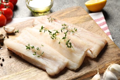 Board with raw cod fish, microgreens and products on grey table, closeup