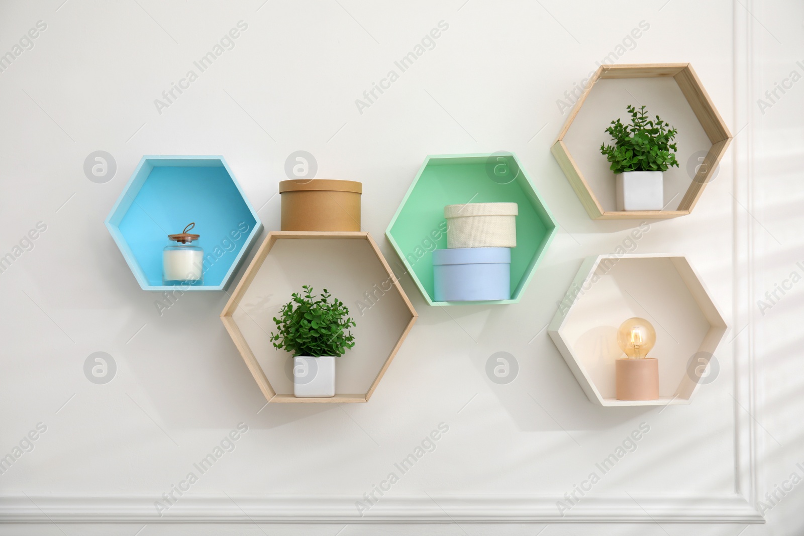 Photo of Honeycomb shaped shelves with decorative elements and houseplants on white wall