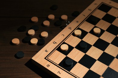 Photo of Checkerboard and game pieces on wooden table, closeup