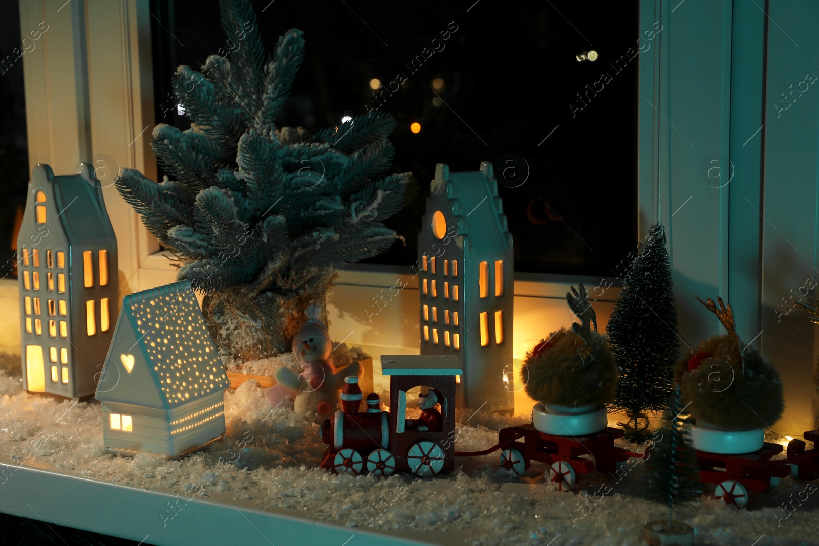 Photo of Christmas atmosphere. Beautiful glowing houses, fir trees, artificial snow and toys on window sill indoors