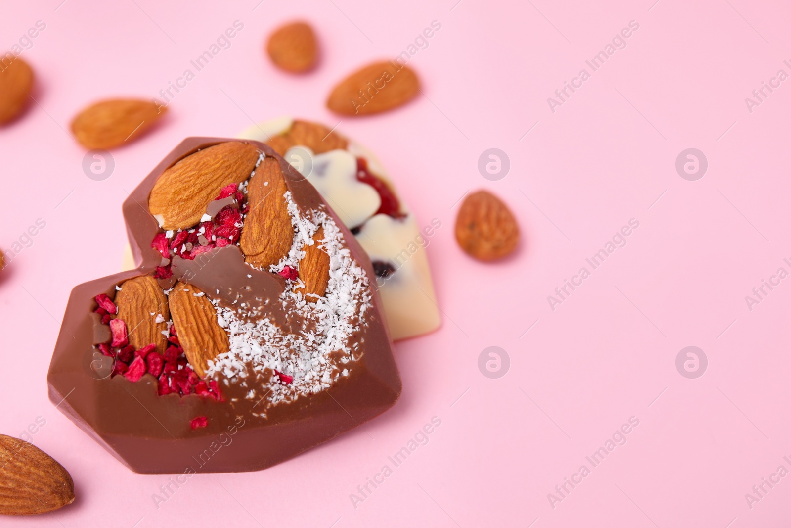 Photo of Tasty chocolate heart shaped candies with nuts on pink background, closeup. Space for text
