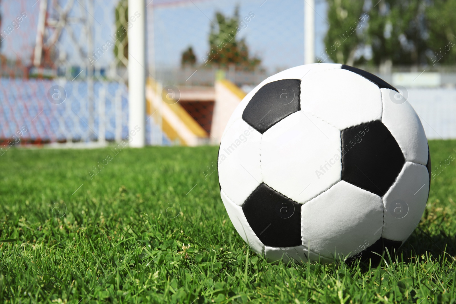 Photo of Soccer ball on green football field grass against net. Space for text