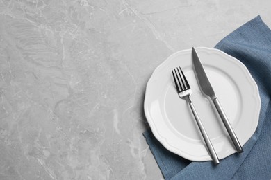Photo of Clean plate with shiny silver cutlery on grey marble table, flat lay. Space for text