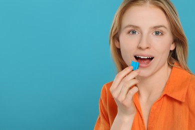 Woman putting bubble gum into mouth on light blue background. Space for text