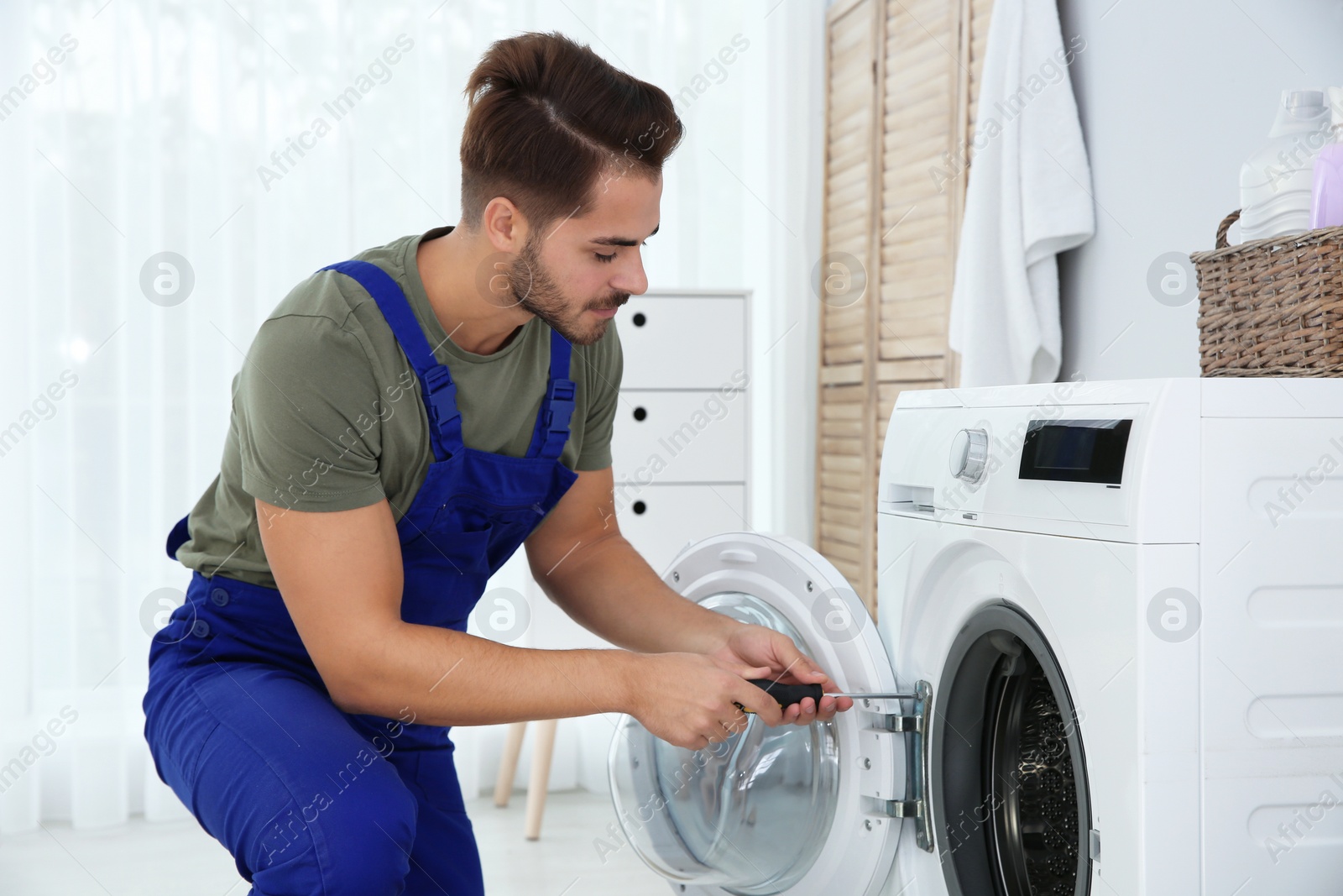 Photo of Young handyman fixing washing machine at home. Laundry day