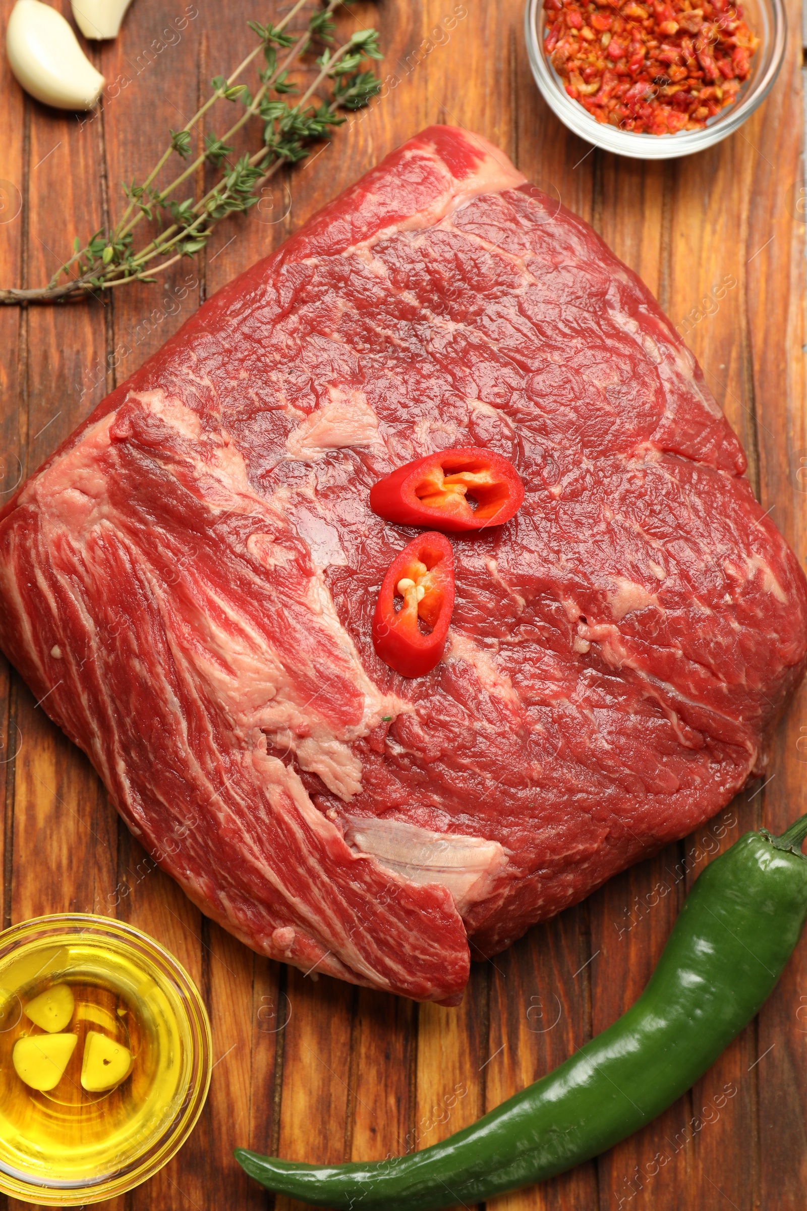 Photo of Fresh raw beef cut, spices and oil on wooden table, flat lay