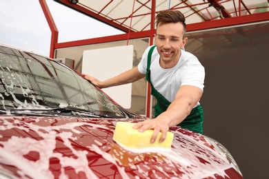 Male worker cleaning vehicle with sponge at car wash